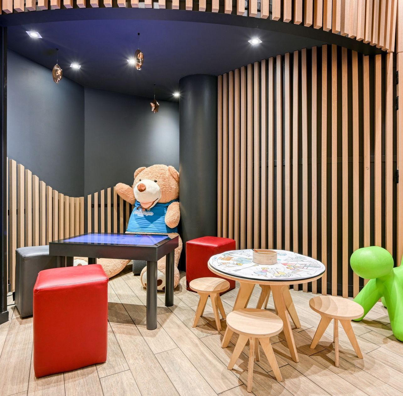 Coin enfant avec tables, chaises et ours en peluche.